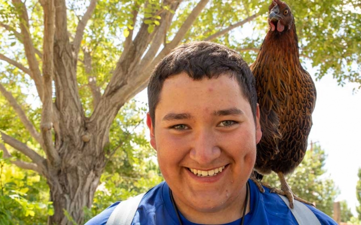 A person smiles at the camera, with a chicken perched on their shoulder.